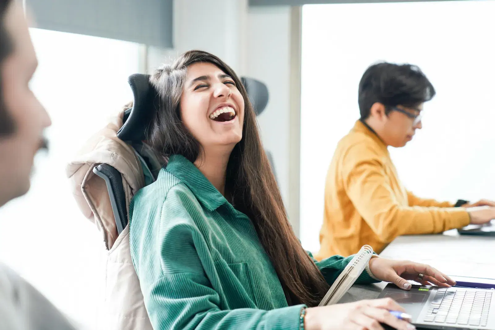 A woman laughing at a laptop with a coworker nearby